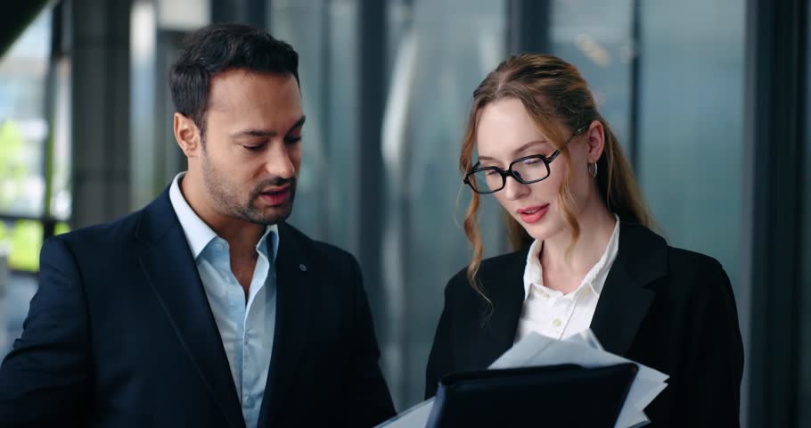 Secretary shows project documents to her boss for review and businessman executive gives feedback standing in modern office - slow motion, parallax shot