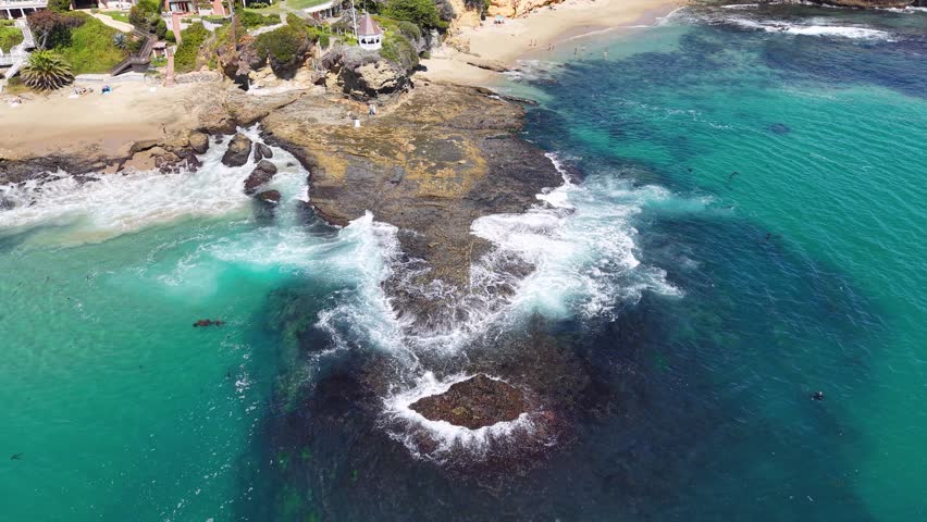 Top-down aerial shot of ocean waves washing over a rocky reef along a coastal shoreline, with shallow turquoise water and visible underwater rock formations