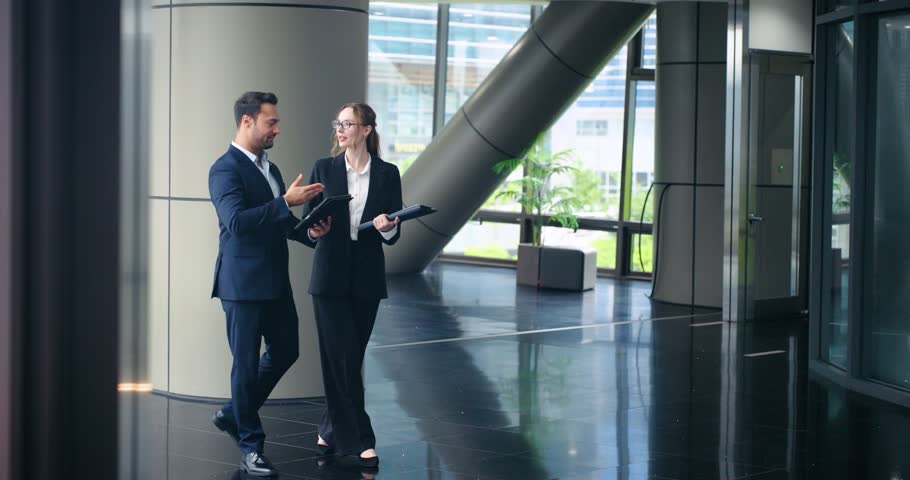 Professional business colleagues man and woman discuss work while walking through modern office lobby tracking slow motion shot