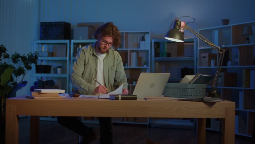 Remote Work and Productivity. A Mature Professional Works Late at Night with Documents and Laptop, Symbolizing Deadlines, Research, and the Challenges of Maintaining Focus in Modern Remote Work.