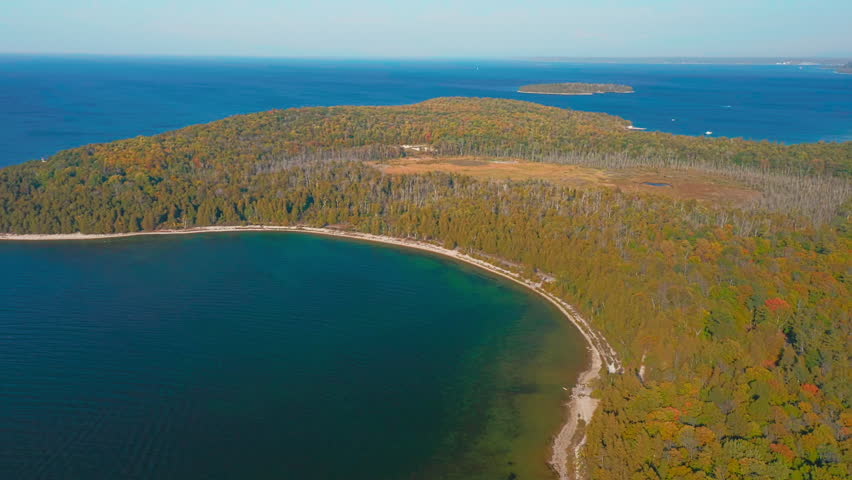 The Door County peninsula stretches between emerald shallows and deep blue lake water, where autumn forests meet the calm horizon of Lake Michigan under clear skies.
