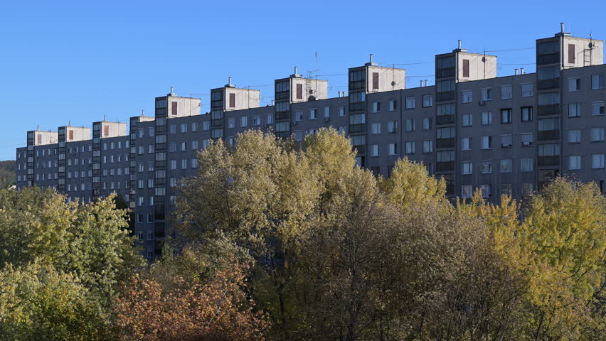 Brutalist apartment buildings behind autumn trees under blue sky
