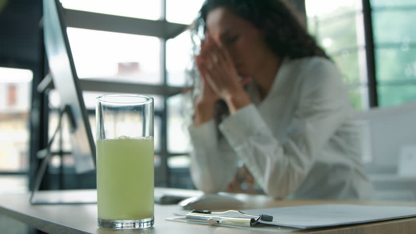 Close-up glass with remedy water medication pill blurred business woman feeling headache pain with computer in office ill sick tired bad feeling businesswoman female girl worker with liquid painkiller