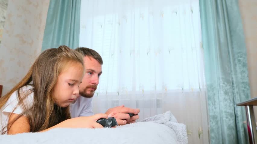 father and daughter are sitting on the couch in their living room, engaged in a competitive video game.