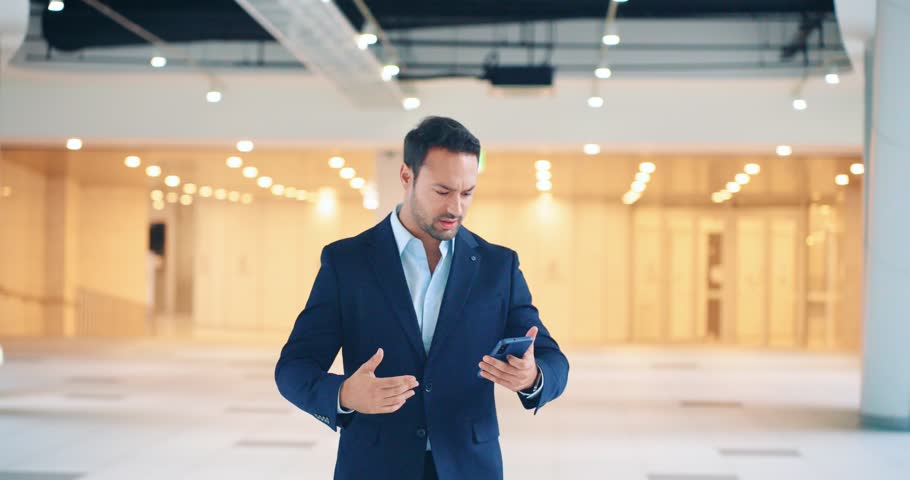 Excited businessman gets big good news on phone call and celebrates his victory by dancing and fist pumping in modern spacious hall - dolly back slow motion