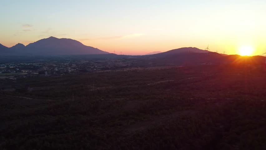 aerial footage showcasing a vibrant sunset over the mountainous landscape on the road to the historic Knidos Ancient City in Turkey. The golden hour light bathes the rolling hills and distant mountain