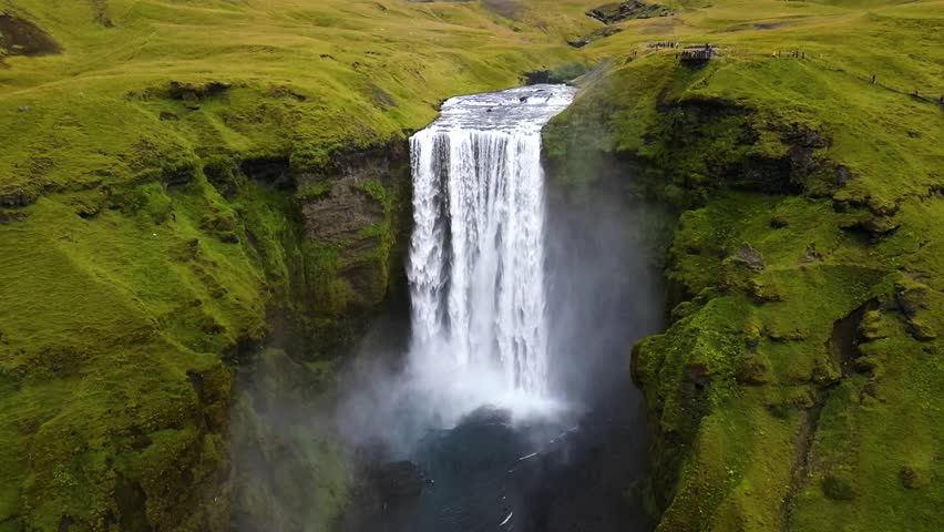 4K cinematic drone footage of Skógafoss Waterfall in Iceland, capturing the immense curtain of water cascading from towering cliffs surrounded by lush green landscapes. Iceland_26