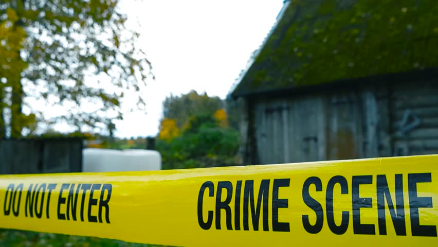 Close up view of a yellow police line or crime scene forensic investigation tape in front of an old vintage countryside farmhouse with autumn trees around with yellow leaves, Bokeh blurry background.