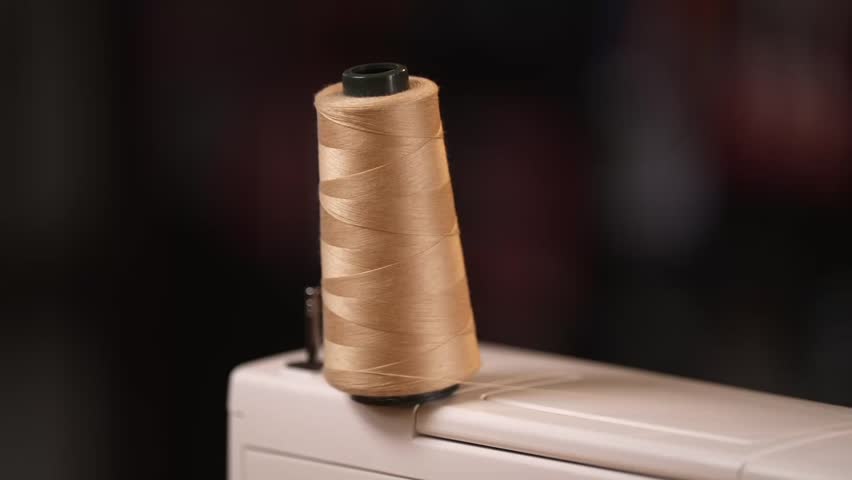 A spool of beige thread sits on a sewing machine, ready for stitching. A minimal, focused look at textile craftsmanship and handmade production.