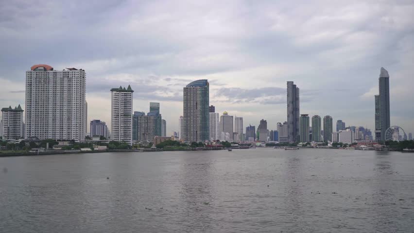 Modern city skyline of Bangkok, Thailand with tall skyscrapers and their reflections on water under a cloudy sky. Urban architecture and cityscape view.