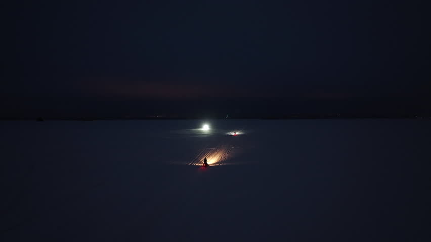 Aerial view of snowmobiles driving on a frozen lake, winter night in Lapland