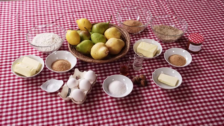 Flat lay of fresh pears, flour, eggs, butter, sugar, nuts, and spices arranged on a red gingham tablecloth, prepared for baking a traditional pear dessert or cake. - Powered by Shutterstock - Get 15% off with code: PIKWIZARD15