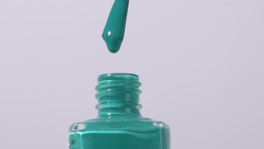 Close-up of blue glossy nail polish dripping from a brush into a jar on a gray background. Concept of nail polish refers to a cosmetic product used to color and protect fingernails and toenails.