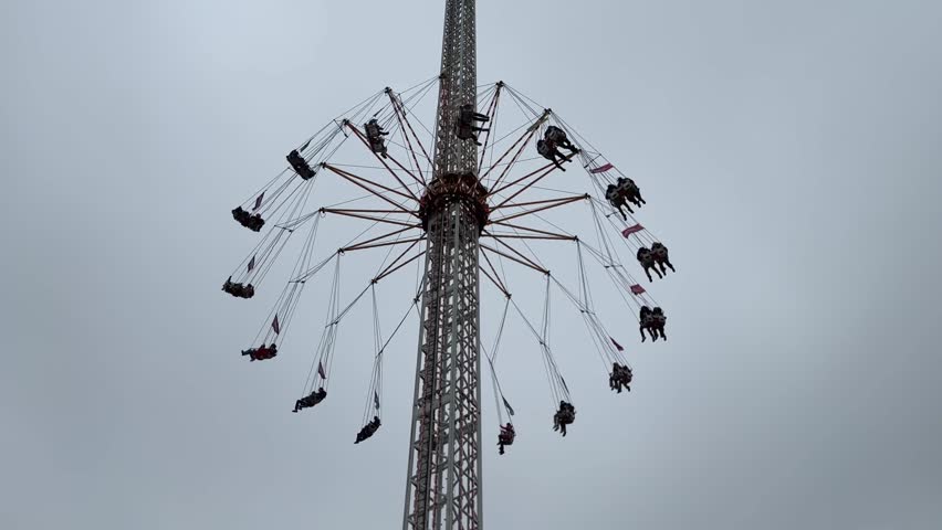 Wide upward shot of a tall amusement park swing carousel rotating with people flying through the air under an overcast sky in Leiden during Leidens ontzet on the 3th of October.