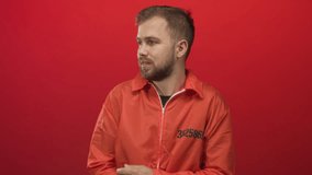 Man prisoner clutching his arms and bracing himself wearing an orange jumpsuit in a red studio; vulnerability. - Powered by Shutterstock - Get 15% off with code: PIKWIZARD15