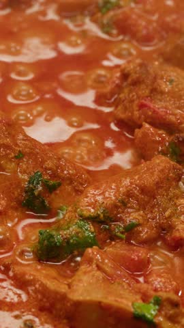 Cooking chicken Indian curry, tikka masala, chicken, lamb, mutton Rogan Josh grill boiling on pan, sauce. Dark background. Close up.