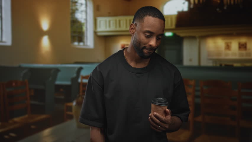 Man holding a takeaway coffee cup with bare hands in a church building, looking upward in soft light; reflection.
