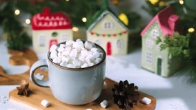 Warm mug of cocoa with marshmallows and festive ceramic village houses and pine cones - Powered by Shutterstock - Get 15% off with code: PIKWIZARD15