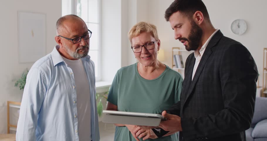 Realtor and real estate agent guides senior couple using tablet a consultation, reviewing a contract at their home and offering advice on meeting. Finacial advisor consult elderly family.