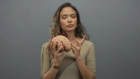 Woman holding a brain model, isolated on a grey background, displaying thoughtful facial expressions, showcasing education, learning, and scientific curiosity. - Powered by Shutterstock - Get 15% off with code: PIKWIZARD15