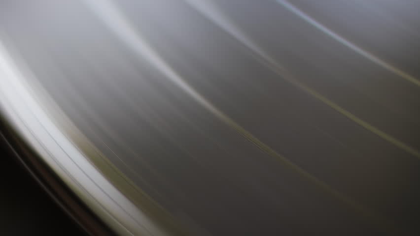 Close-up view of a black vinyl record spinning on a turntable. The grooves reflect light, creating a hypnotic and classic visual