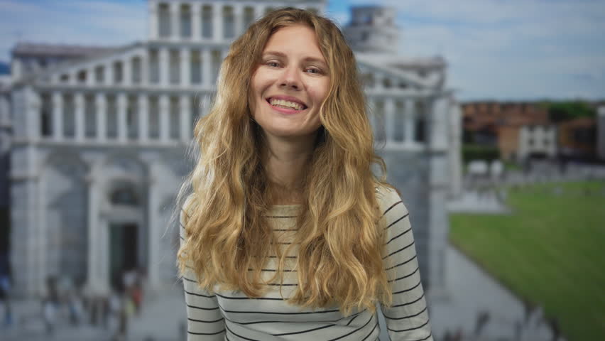 Woman raises her hand before pointing to pisa plaza while blonde young smiling tourist adores the leaning tower landmark.