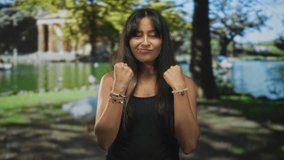 Woman holding fists up in a boxing pose at a park by a pond; confidence empowerment resilience determination. - Powered by Shutterstock - Get 15% off with code: PIKWIZARD15