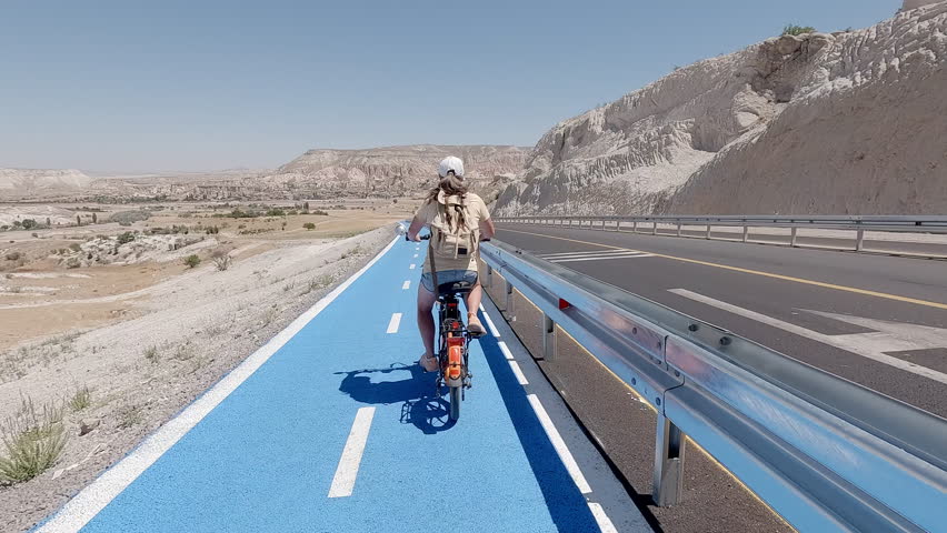 Woman tourist rides bicycle along bike path in Cappadocia, exploring unique landscapes of mountain valley