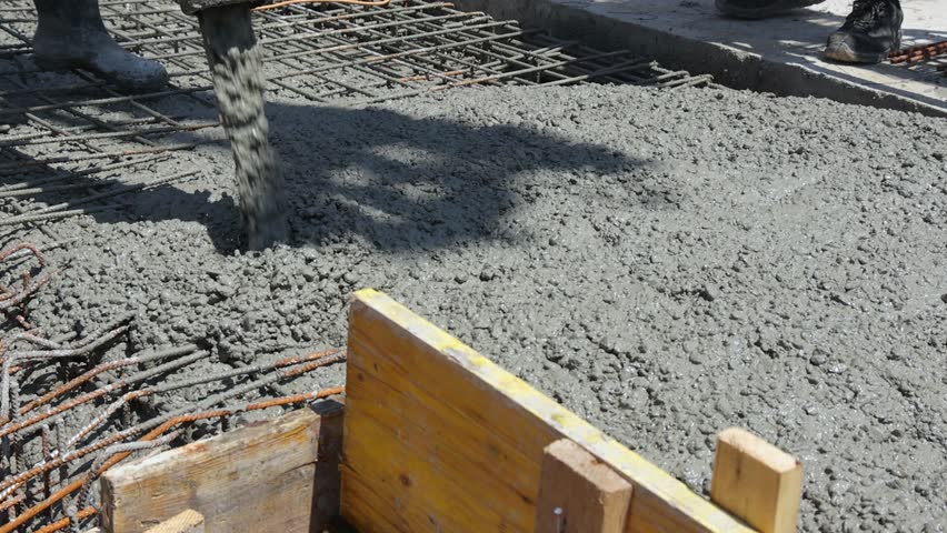 Construction workers with concrete boom pump crane at construction site pouring concrete and leveling fresh concrete floor with a wooden tool building a new house
