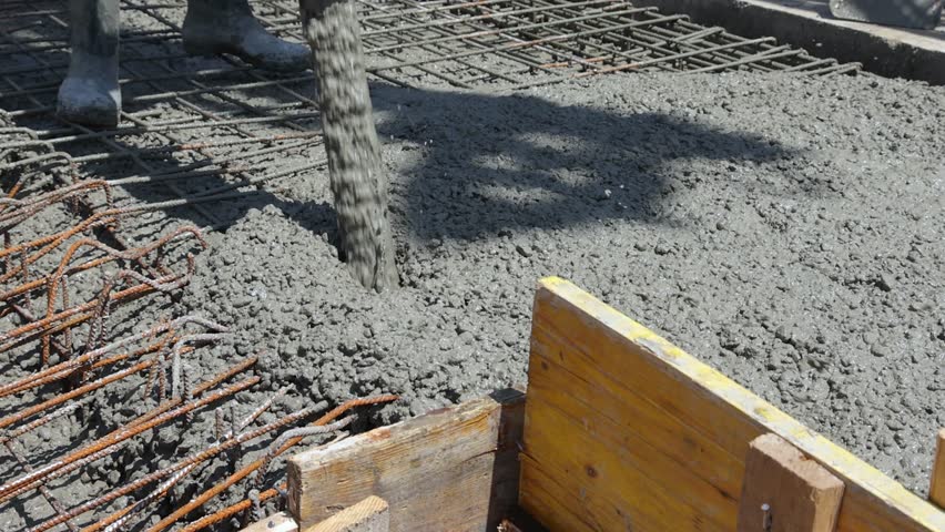 Construction workers with concrete boom pump crane at construction site pouring concrete and leveling fresh concrete floor with a wooden tool building a new house