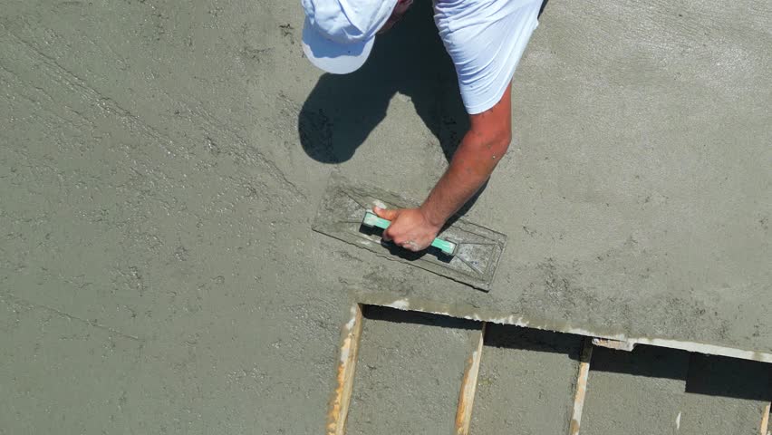 Construction worker are using finishing trowels on freshly poured concrete to create a smooth, level surface at a building site. View from above shows worker leveling the surface of the stairs