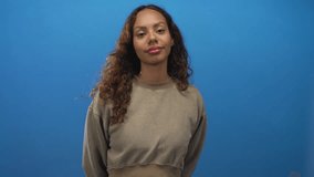 Young african american woman standing with hands behind back showing relaxed face and closed eyes in studio with blue backdrop; quiet contentment. - Powered by Shutterstock - Get 15% off with code: PIKWIZARD15
