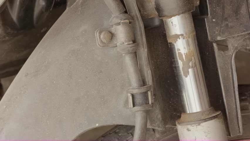A close-up shot of a mechanic using a tool (possibly a cutter or sharp scraper) to clean dirt, grime, or rust buildup from the shiny chrome shaft of a motorcycle's front shock absorber