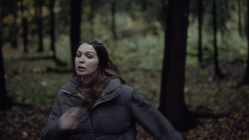 Frightened woman turning around while running in dark autumn forest
