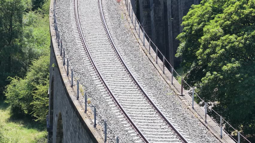 Empty train tracks curve along a viaduct on a sunny summer day, offering a scenic view of railway infrastructure
