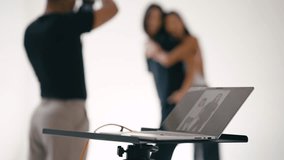 Professional photographer taking pictures of fashion models in a studio with a white background, using a laptop to review the shots - Powered by Shutterstock - Get 15% off with code: PIKWIZARD15