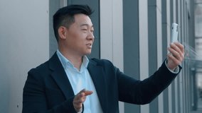 Asian business man talking video call in city with mobile phone chat Korean 40s businessman male talk online internet conference using smartphone Chinese Japanese employer communicate negotiation - Powered by Shutterstock - Get 15% off with code: PIKWIZARD15