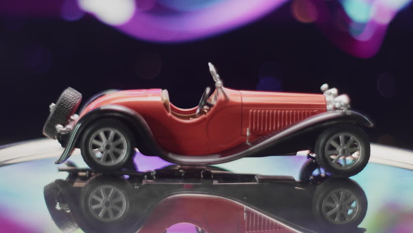 Old toy red model car showcased under colorful lights at a fair
