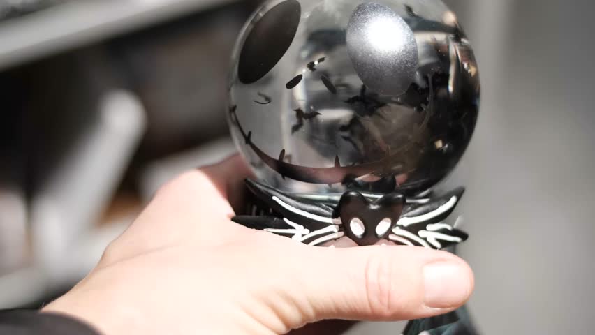 A dark crystal ball with spooky eyes and spider base held inside a Halloween-decorated retail environment 
