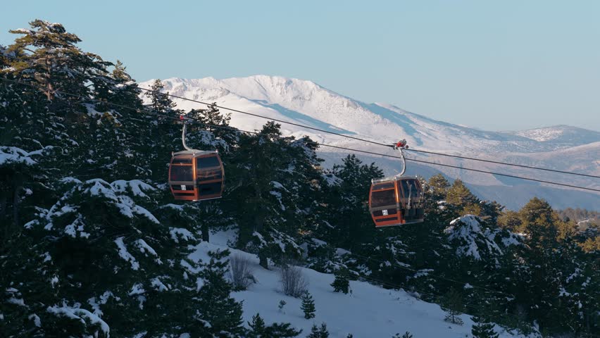 Aerial drone footage of ski gondolas moving through a snowy forest on a mountain slope. A peaceful winter landscape combining nature, tourism, and adventure.
