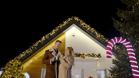 A man and woman share a warm drink in front of a beautifully decorated house during the holiday season - Powered by Shutterstock - Get 15% off with code: PIKWIZARD15