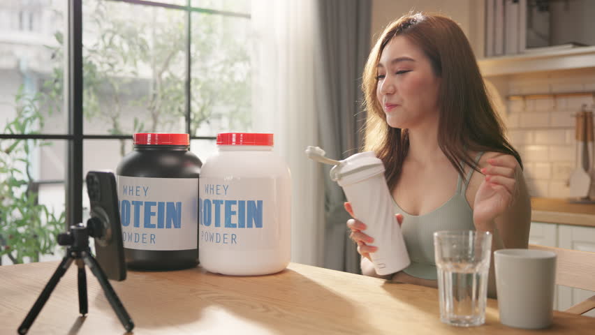 Young Asian female health influencer live streaming on social media sharing nutrition tips with whey protein powder by smartphone. Healthy lifestyle, fitness coaching, clean eating. online marketing.
