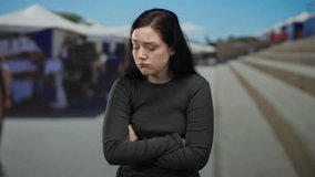 Woman standing on street outdoors with crossed arms and serious expression in front of blurred background, brunette hair, casual attire. - Powered by Shutterstock - Get 15% off with code: PIKWIZARD15