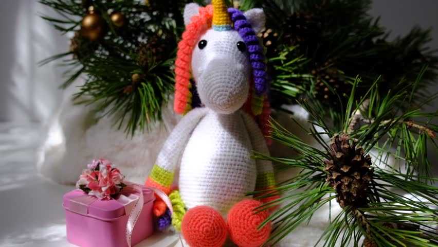 Cute unicorn toy with gift box. New Year decorations toys. Christmas atmospheric mood. Blurred, softness, golden flares. Merry Xmas concept. Happy holidays for child.