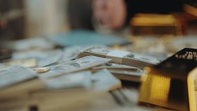 Male hands counting a large sum of money on a table, surrounded by stacks of hundred-dollar bills, gold coins, and bitcoin, symbolizing wealth, investment, and financial success - Powered by Shutterstock - Get 15% off with code: PIKWIZARD15