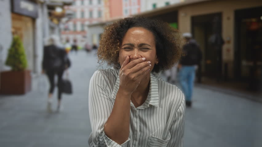 Woman hand covering mouth on street with passersby and storefronts in view; surprise candid reaction.