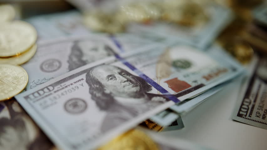 Slow motion closeup of shiny golden bitcoins falling onto a pile of united states one hundred dollar bills, representing digital currency investment, wealth accumulation, and modern finance - Powered by Shutterstock - Get 15% off with code: PIKWIZARD15