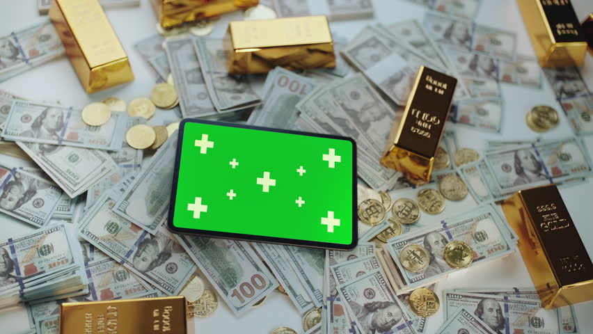 Digital tablet with a green screen and tracking markers slowly zooming in. Lying on a background of one hundred dollar bills. Bitcoin coins. And gold bars. Representing financial technology concepts