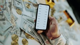 Close-up of a hand holding a smartphone, scrolling through a finance application and then subscribing to a channel, with a background of cash, gold bars, and cryptocurrency coins - Powered by Shutterstock - Get 15% off with code: PIKWIZARD15
