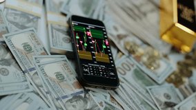 Mobile phone displaying a cryptocurrency or forex trading candlestick chart on its screen, surrounded by a large amount of us hundred-dollar bills, bitcoins, and gold bars - Powered by Shutterstock - Get 15% off with code: PIKWIZARD15